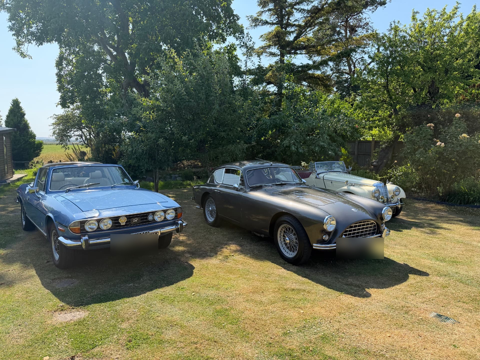 A blue Triumph Stag, a grey AC Aceca-Bristol and a cream MG TF1500 parked together on a lawn