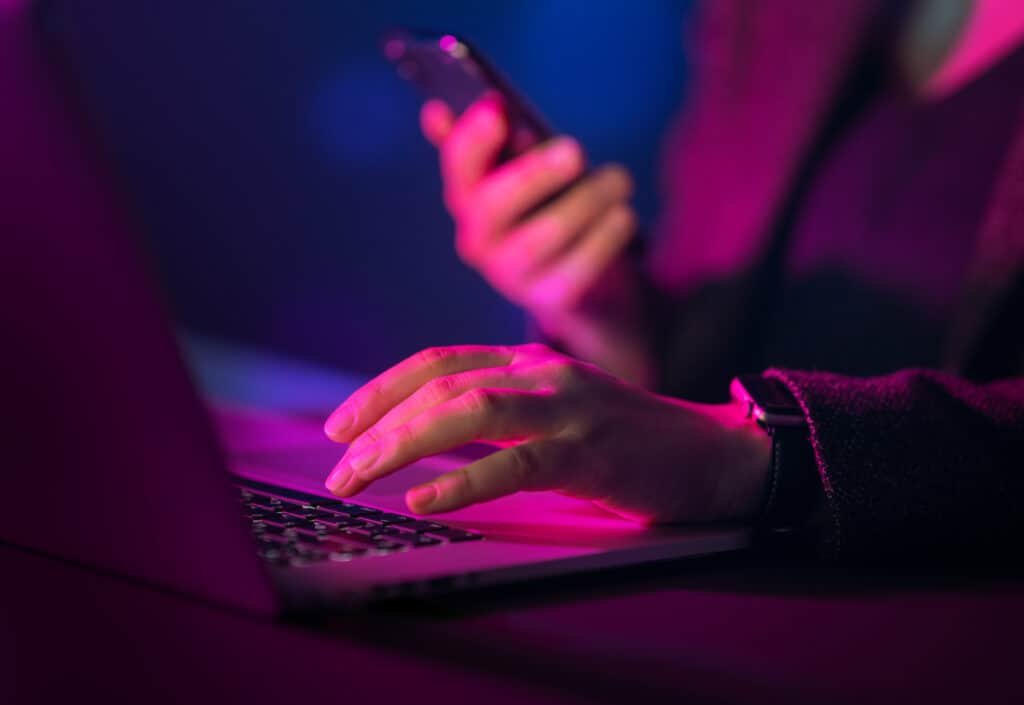 Cybercriminal using laptop, and hands close up orchestratiing a Smishing attack.