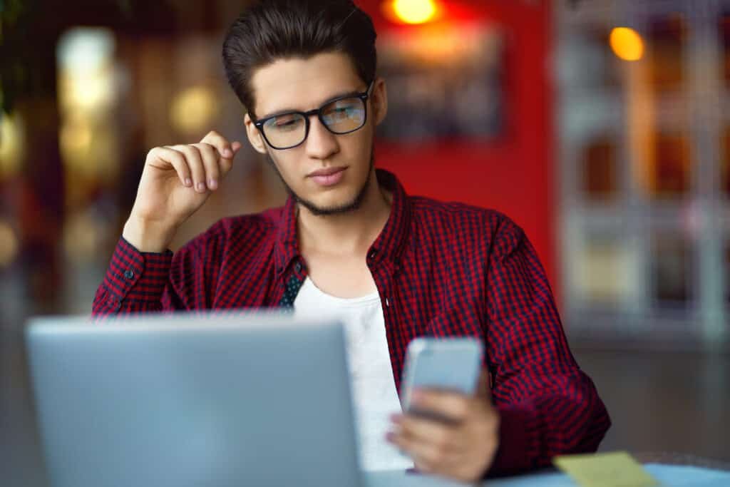 Man checking his phone and laptop referencing his passwords