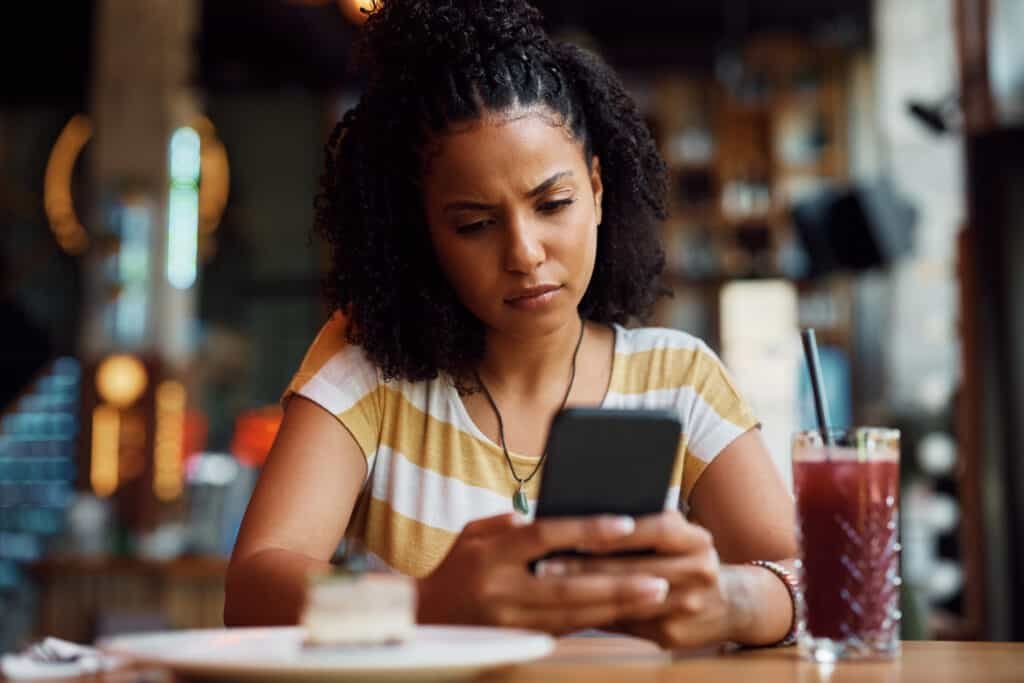 A pensive woman tusing her smart phone while sitting alone in a cafe.