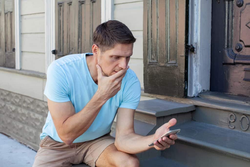 Man checking phone concerned he has been scammed by the royal mail fee to pay scam