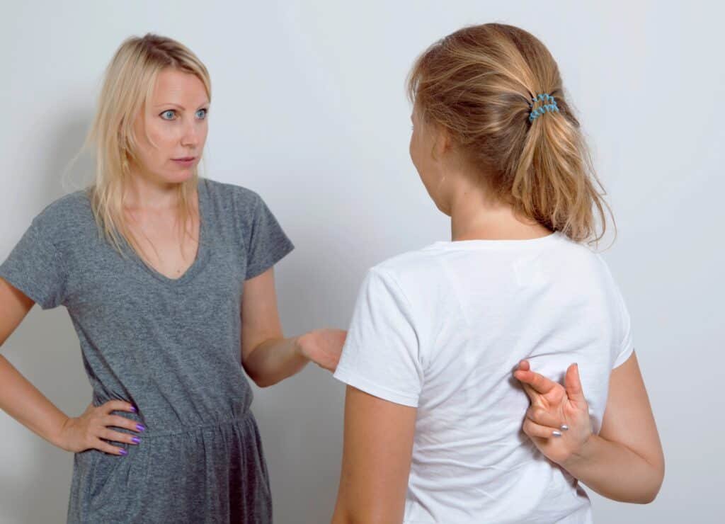 A mother and a child discussing online activity with the child hiding her crossed fingers behind her back