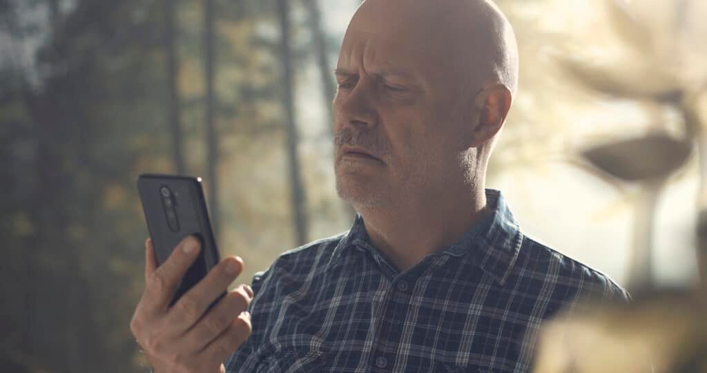 A man walking in a forest and trying to connect online with his smartphone.