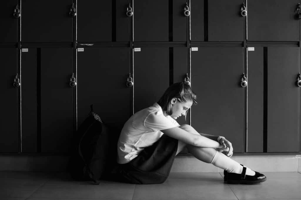 A distressed girl sitting on the floor at school by a series of lockers