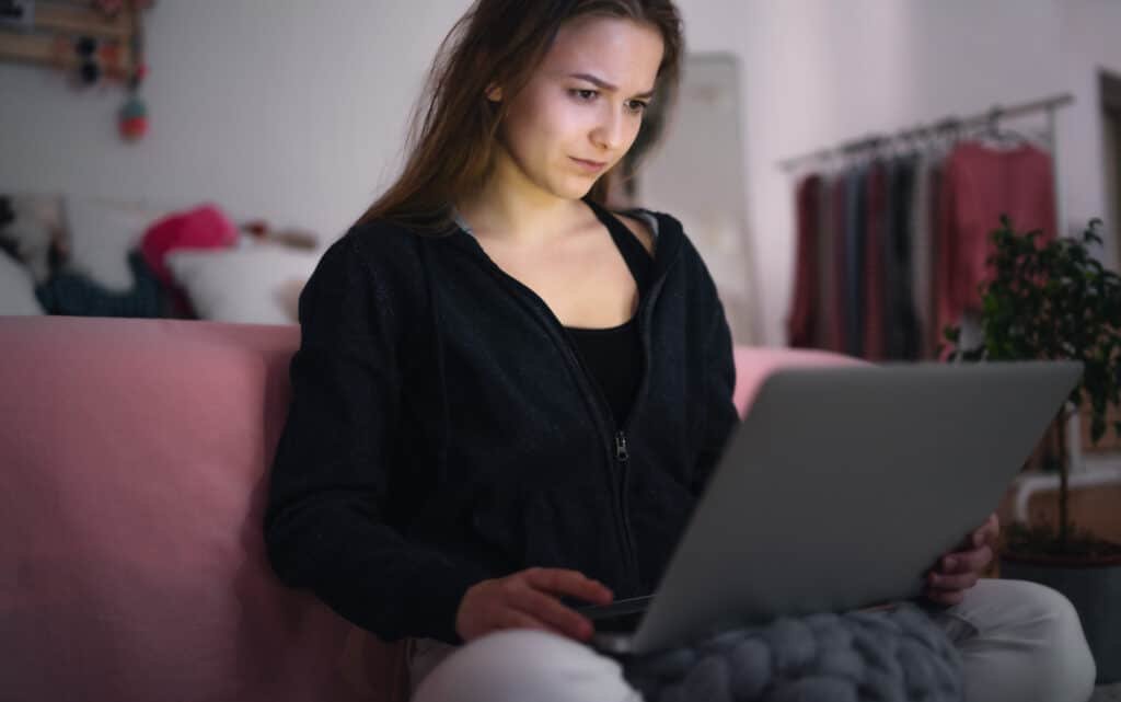 Young woman on a laptop sitting on a sofa checking fake webites