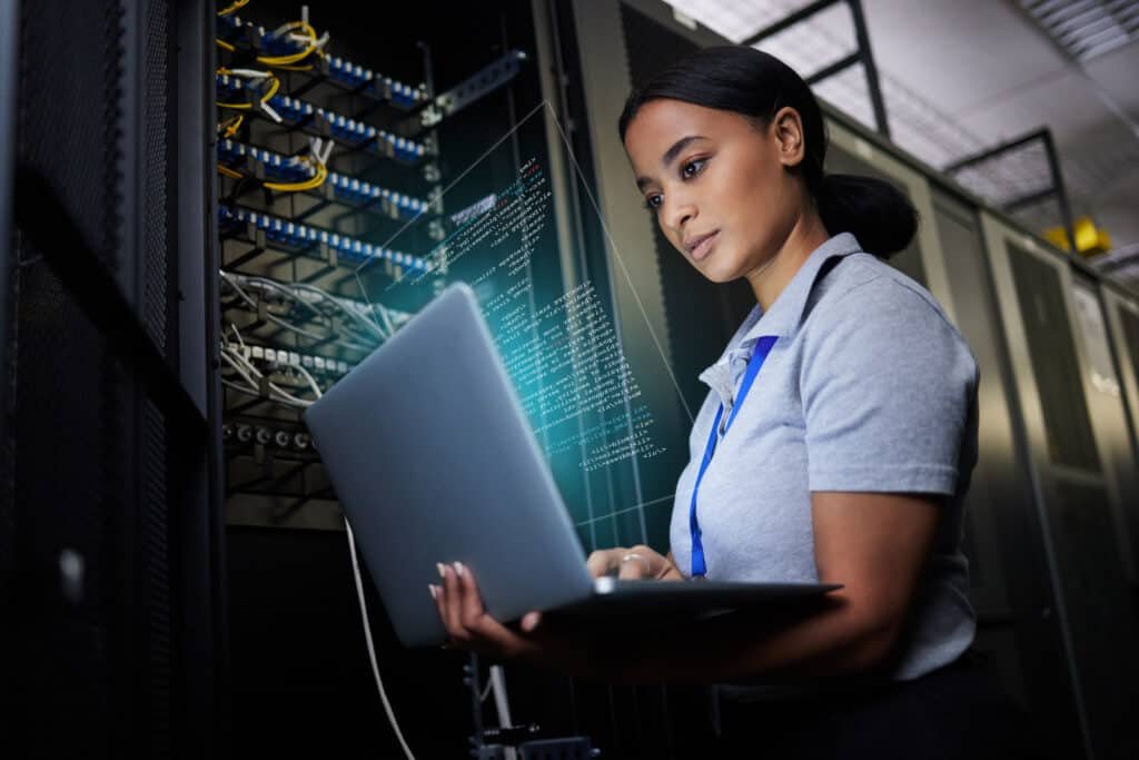 A woman Cyber Security engineer working in young a datacentre on a Laptop connected to a network to resolve an issue