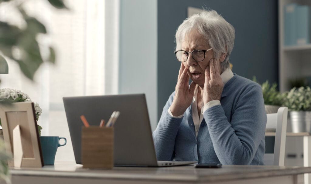 Senior woman struggling with technology, she is confused and staring at the computer screen potentially being scammed by Wilko website