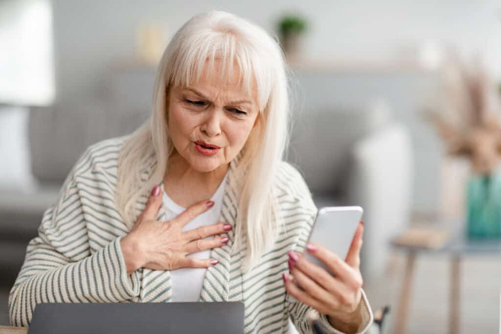 Shocked Mature Woman Looking At Smartphone Screen With Open Mouth, Touching Chest In Amazement And Surprise of Cyber Fraud and social media scams