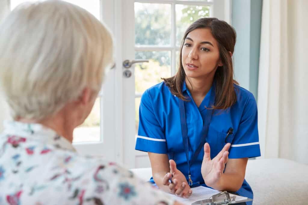 Senior woman talking to young care nurse on home visit about NHS scams