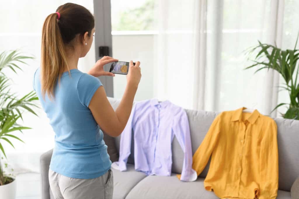 Woman taking a picture of her used shirts with her smartphone, she is selling clothes online