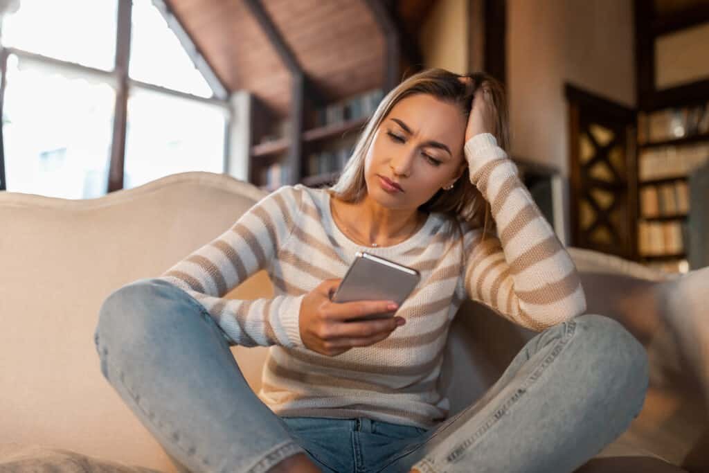 Woman Holding Smartphone, Looking At Mobile Phone Screen With Worried Expression as she has clicked on a Netflix Scam email