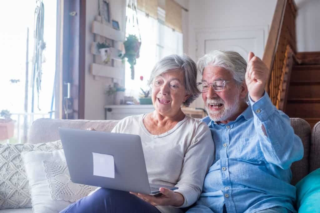 Overjoyed mature couple looking at laptop screen, celebrating online lottery win, not knowling it was a postcode lottery scam