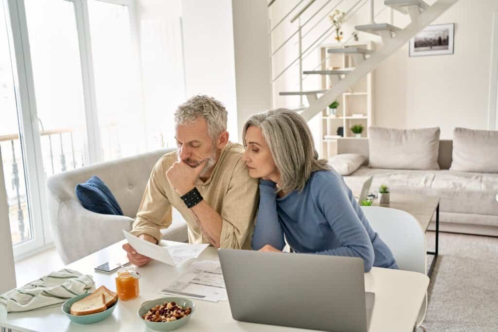 Worried old senior couple checking bank documents at home as they are concerned about financial crime