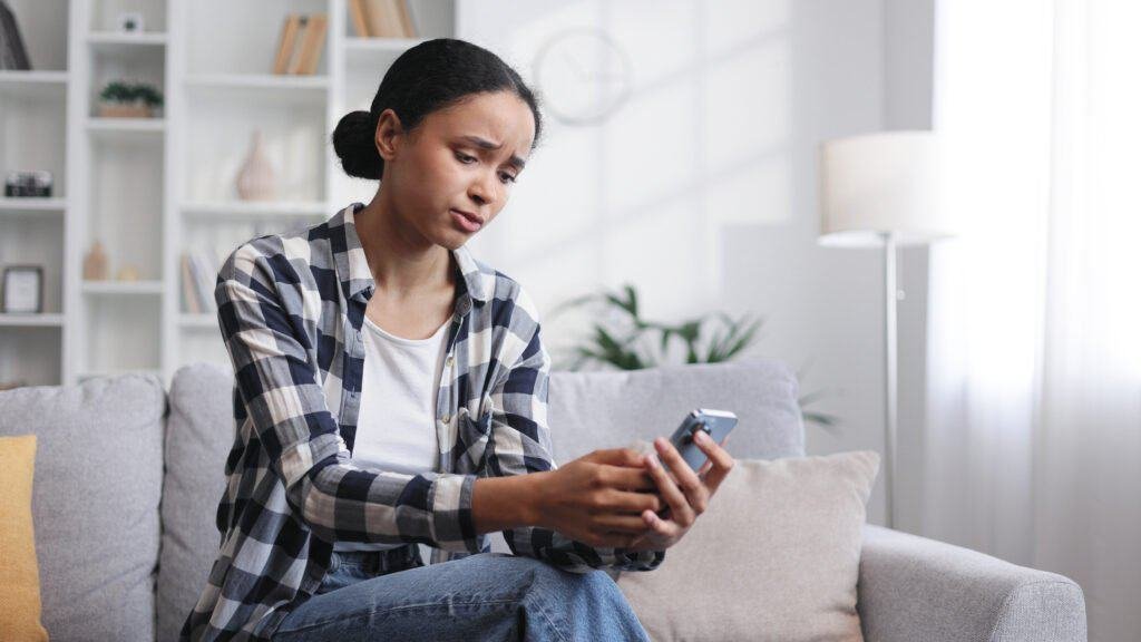 Concerned girl sitting on the sofa looking at her phone recieving messages from potential BT Scams
