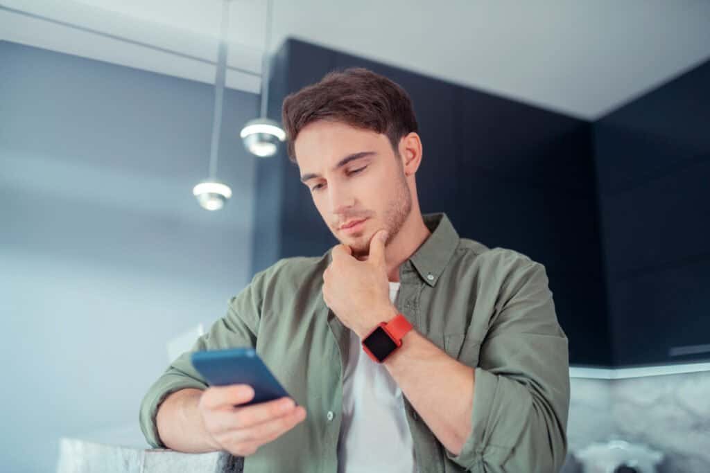 Young man wearing smart watch feeling thoughtful while reading e-mail from a fake postcode lottery scam communication