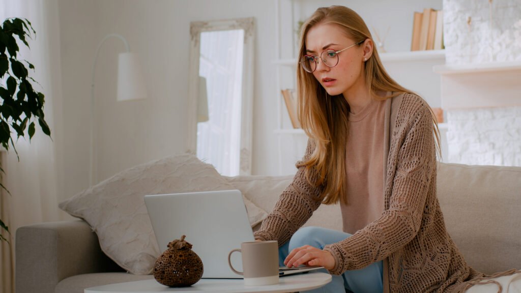 A shocked blonde girl in glasses looking serious as she locks her laptop and proteting herself from Fedex scam emails.