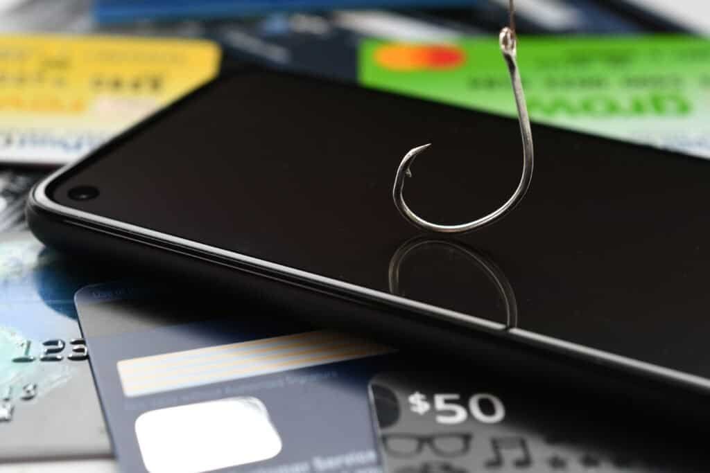 Smart phone laid on a series of credit cards with a hook dangling on top of the device - used to denote Called ID Spoofing