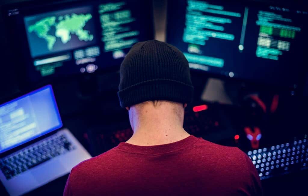 Rear view of a cyber criminal working on various computers commiting cyber fraud
