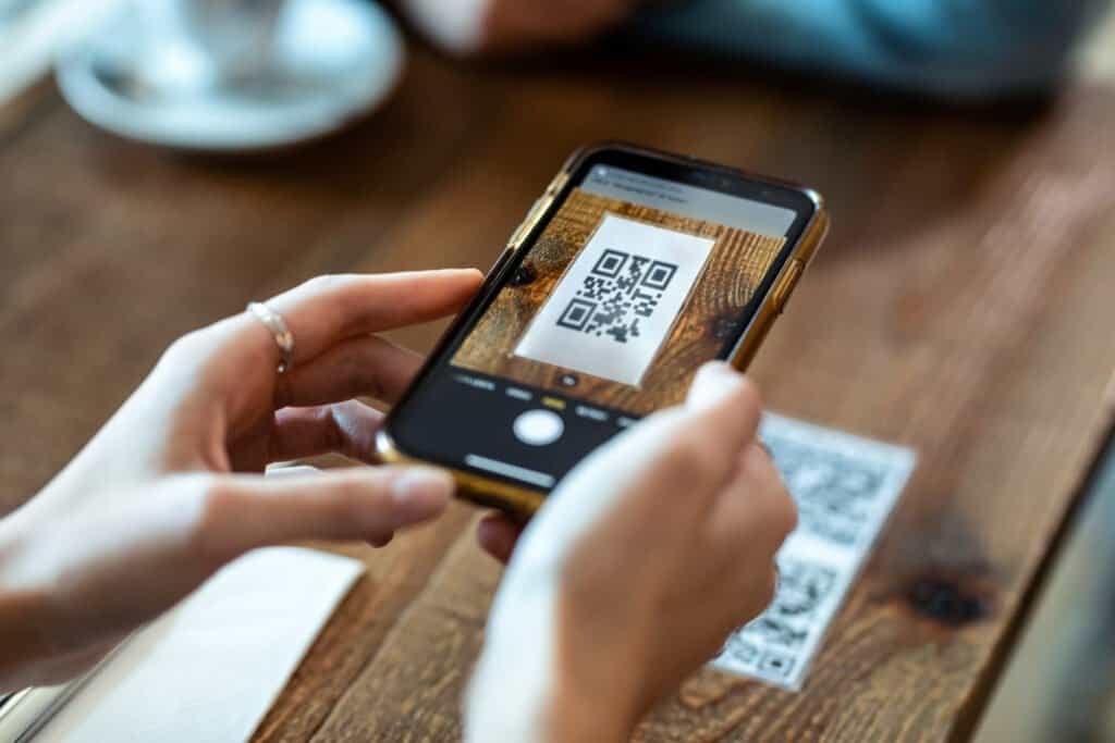 Close up of young woman hands using the smart phone to scan the qr code to select food menu in the restaurant without checking the validity of the QR Code. This is subject to QR Code Scams.