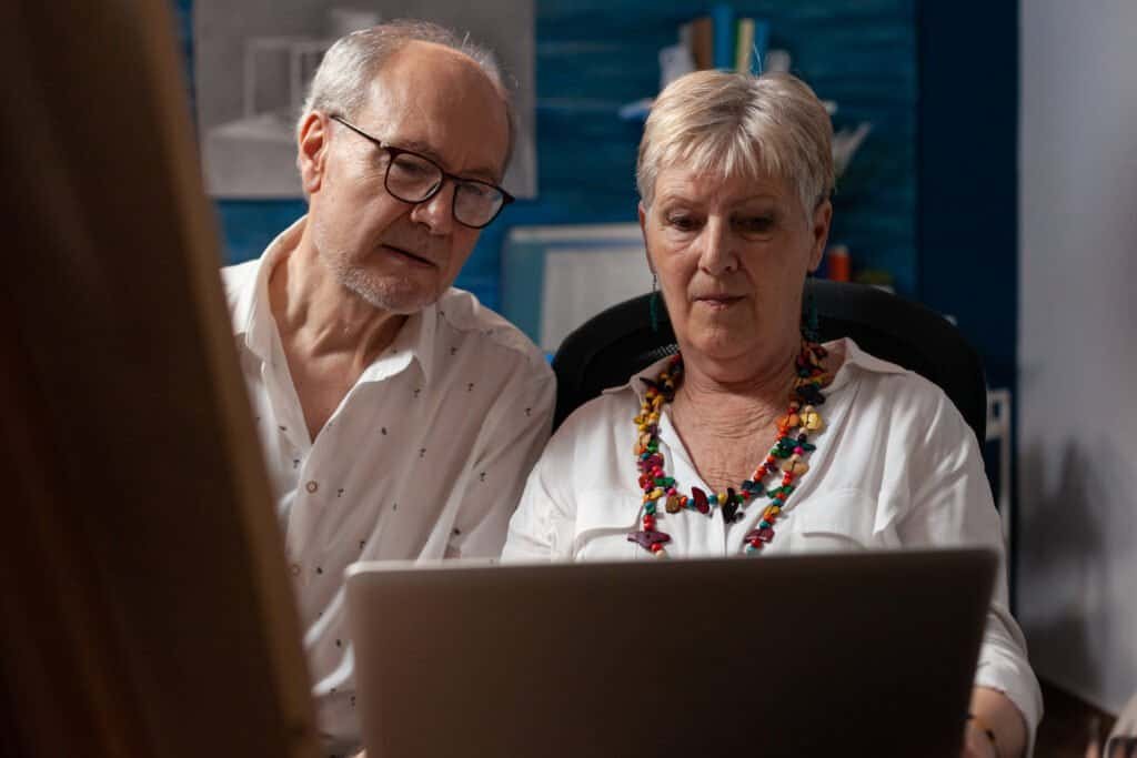 Elderly couple holding laptop looking at screen trying complete a tax return online
