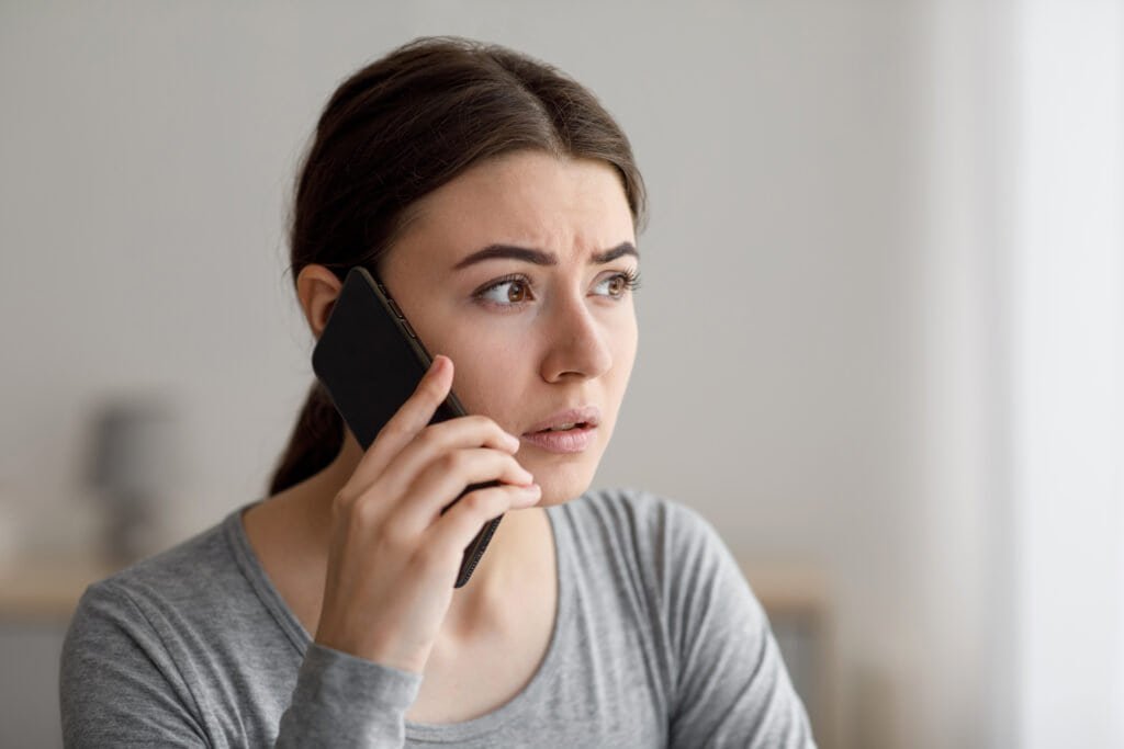 A worried anxious upset millennial lady talks by phone, reporting Vodafone scams to the authorities