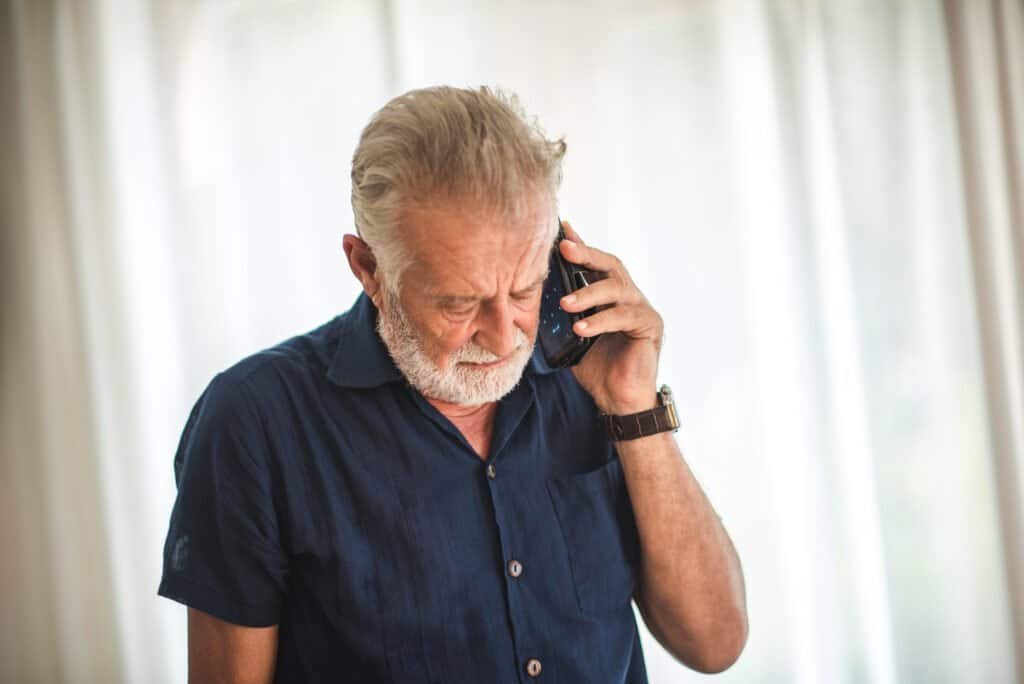A senior man talking on a smartphone, calling his bank to report a Vodafone scams