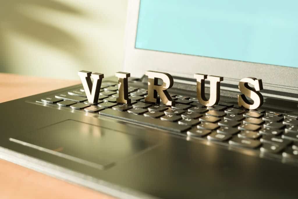 Word VIRUS with wooden vintage letters, laptop keyboard background.