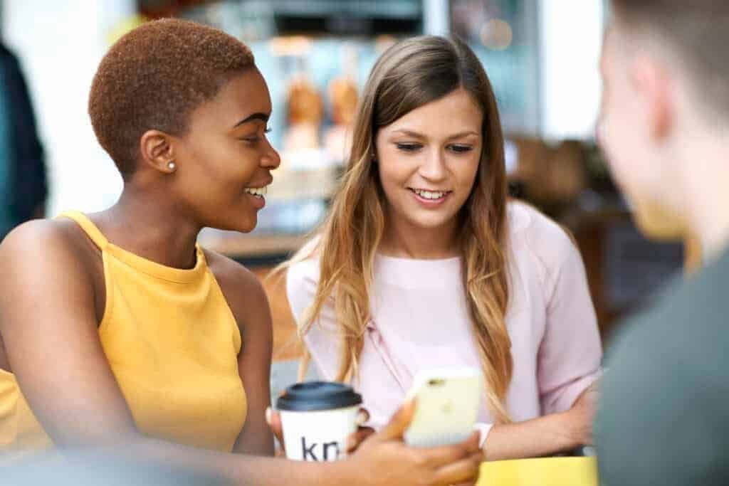 Group of friends, outdoors, looking at smartphone with one girl showing how to secure a Facebook account