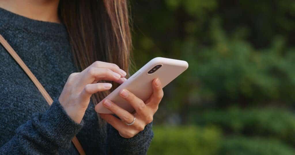 Woman using  a smart phone at a car park to report a Parking App Scam to the authorities.