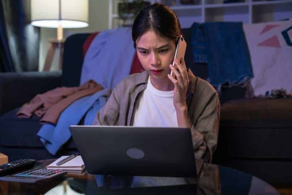 A young woman using her laptop and calling Fedex regarding Fedex Scam emails.